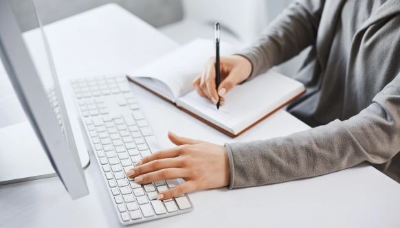 Woman typing on laptop and writing on a notebook