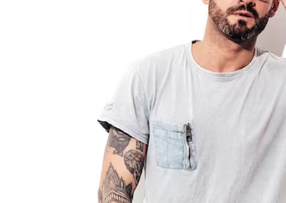 Стоит мужчина татуированный с бородой в серой футболке презентует свободный стиль